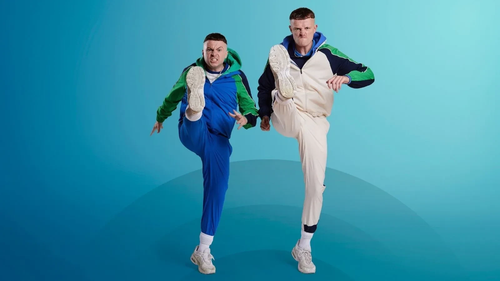 Two men in tracksuits with their legs in the air with humorously angry faces against a blue background
