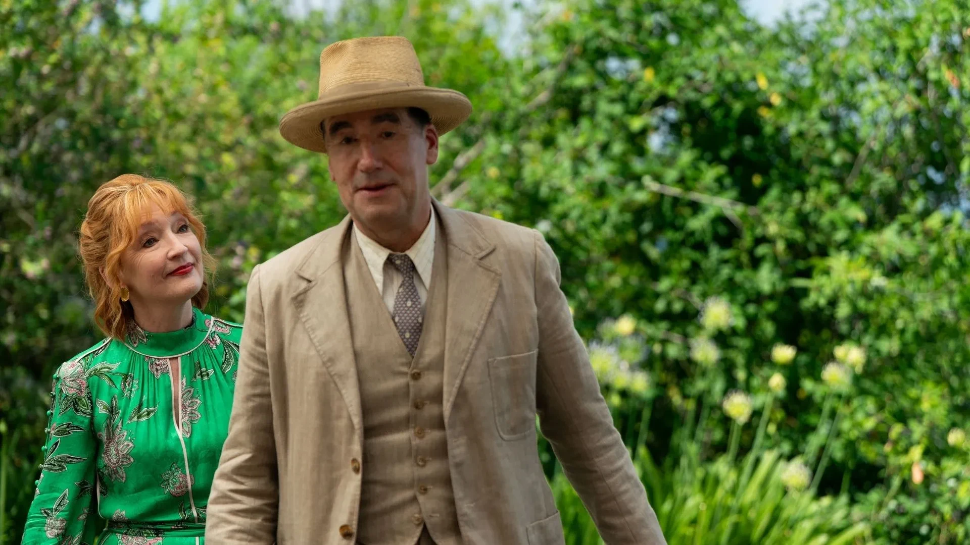Period mystery drama scene from Marble Hall Murders showing two characters walking through a sunlit garden in 1930s attire.