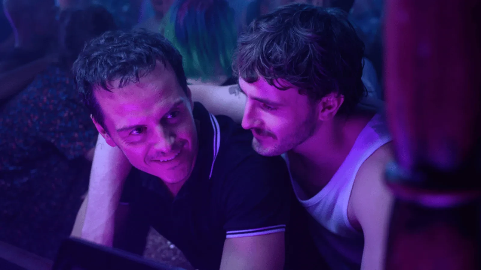 Two men in a purple lit room smiling at each other