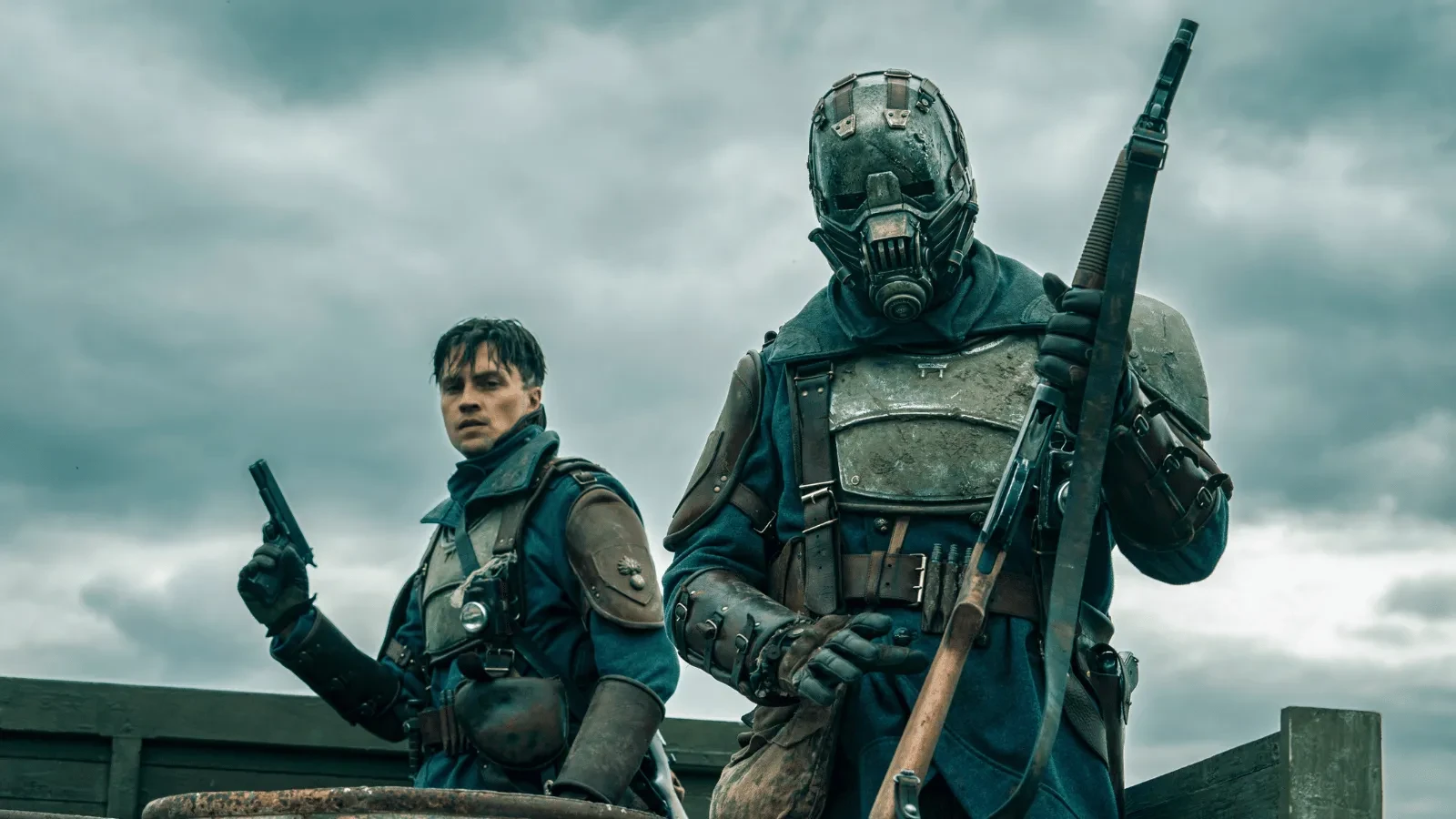 The Sentinels promotional artwork showing two heavily armoured figures carrying weapons in a bleak post-apocalyptic landscape beneath stormy skies.